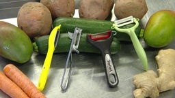Vier verschiedene Gemüseschäler an zwei Zucchinis angelehnt