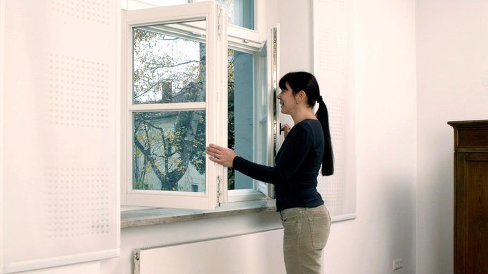 Eine Frau öffnet ein Fenster zum Lüften in einem Zimmer