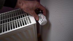 Ein Mann dreht am Thermostat einer Heizung