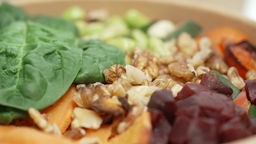Das Bild zeigt eine To-Go-Bowl mit Salat und Nüssen. 