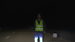 Ein Mann in einer Warnweste steht auf einer dunklen Straße.