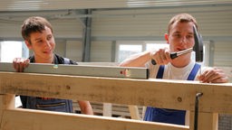 Zwei Auszubildende in einer Schreinerei klopfen Nägel in Holzbalken
