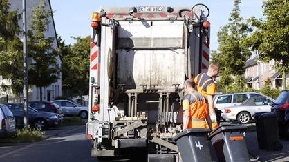 2 Männer der AWB laden Mülltonnen auf einen Müllwagen