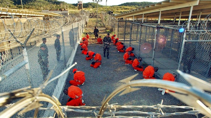 In orangefarbene Overalls gekleidete Häftlinge knien im Camp X-Ray auf dem US-Marinestützpunkt Guantanamo Bay (Aufnahme von Januar 2002)