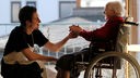 Ein Zivildienstleistender spricht mit einer alten Dame im Rollstuhl