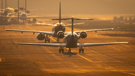 Zwei Flugzeuge von hinten auf einer Landebahn in goldenem Abendlicht.