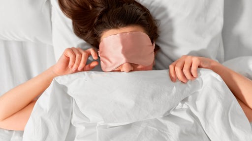 Eine Frau mit rosa Schlafmaske liegt in einem Bett und träumt einen Traum.